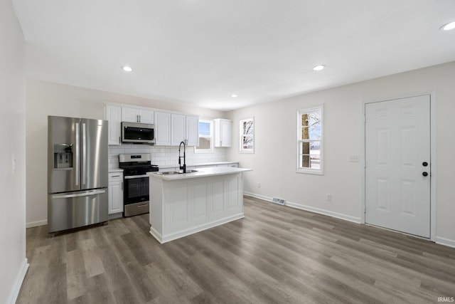 kitchen featuring appliances with stainless steel finishes, tasteful backsplash, sink, white cabinets, and light hardwood / wood-style floors