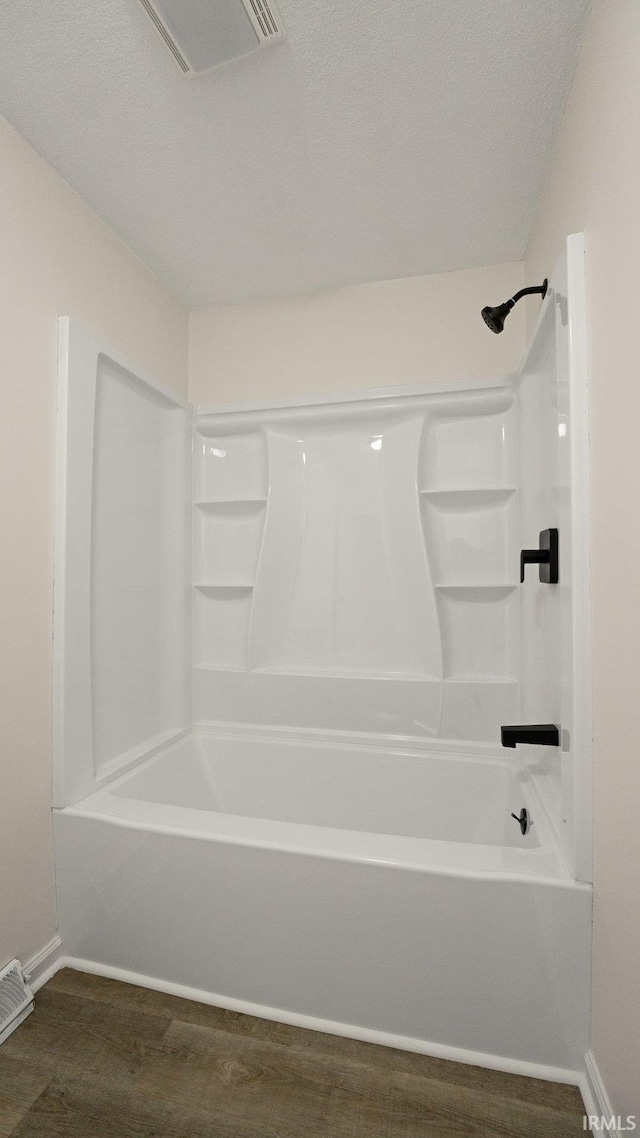 bathroom with a textured ceiling, hardwood / wood-style flooring, and shower / bathtub combination