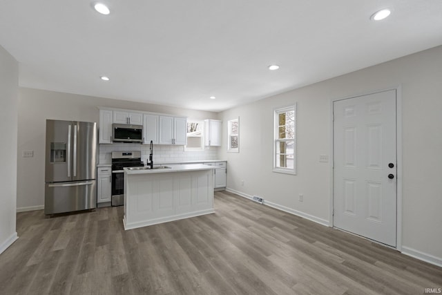 kitchen with appliances with stainless steel finishes, backsplash, a center island, light hardwood / wood-style floors, and white cabinetry