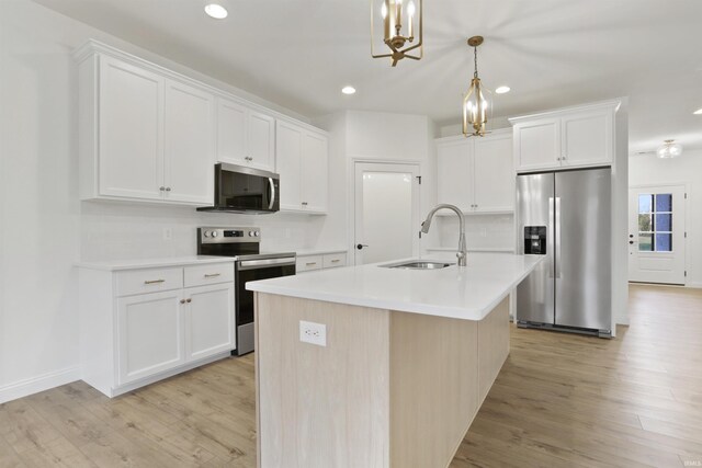 kitchen with sink, an island with sink, decorative light fixtures, white cabinets, and appliances with stainless steel finishes