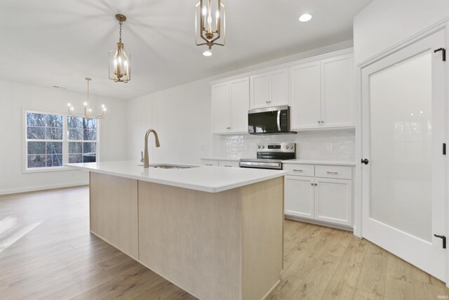 kitchen featuring a kitchen island with sink, hanging light fixtures, appliances with stainless steel finishes, light hardwood / wood-style floors, and white cabinetry