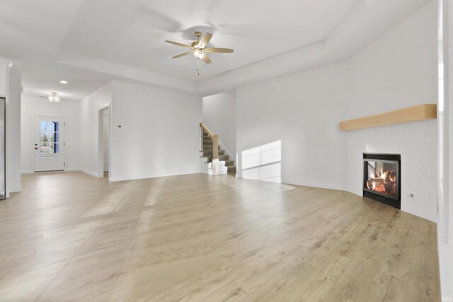 unfurnished living room with a tray ceiling, light hardwood / wood-style flooring, and ceiling fan