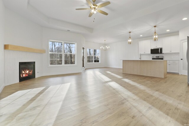 unfurnished living room featuring ceiling fan with notable chandelier and light hardwood / wood-style floors