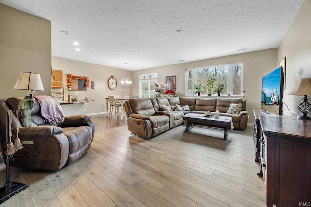 living room featuring plenty of natural light, light hardwood / wood-style floors, a textured ceiling, and a chandelier