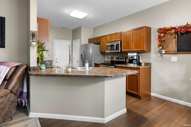 kitchen featuring a breakfast bar, hardwood / wood-style flooring, a textured ceiling, kitchen peninsula, and stainless steel appliances