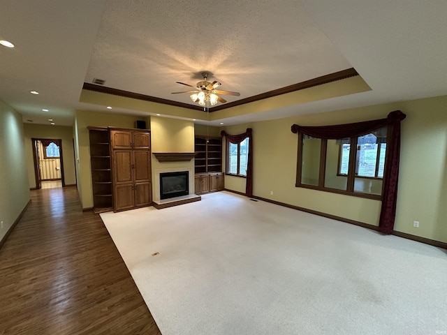 unfurnished living room with ceiling fan, a textured ceiling, a tray ceiling, a fireplace, and ornamental molding