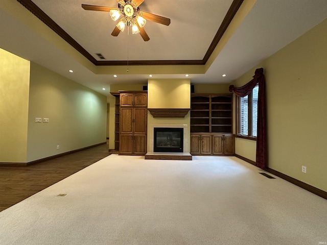 unfurnished living room with a tray ceiling, ceiling fan, ornamental molding, and dark hardwood / wood-style floors