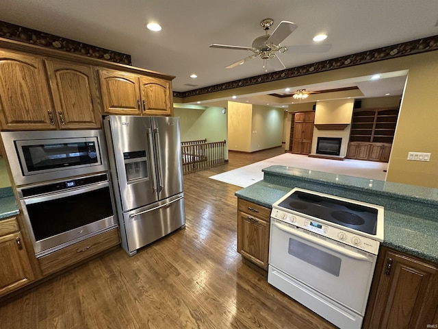 kitchen featuring dark wood-type flooring, ceiling fan, a fireplace, and stainless steel appliances