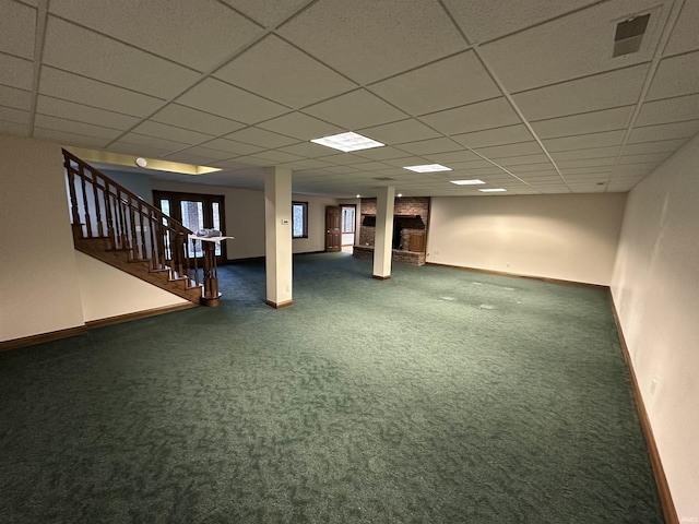 basement featuring dark colored carpet, a paneled ceiling, and a fireplace