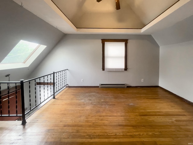 additional living space with baseboard heating, ceiling fan, vaulted ceiling with skylight, and wood-type flooring