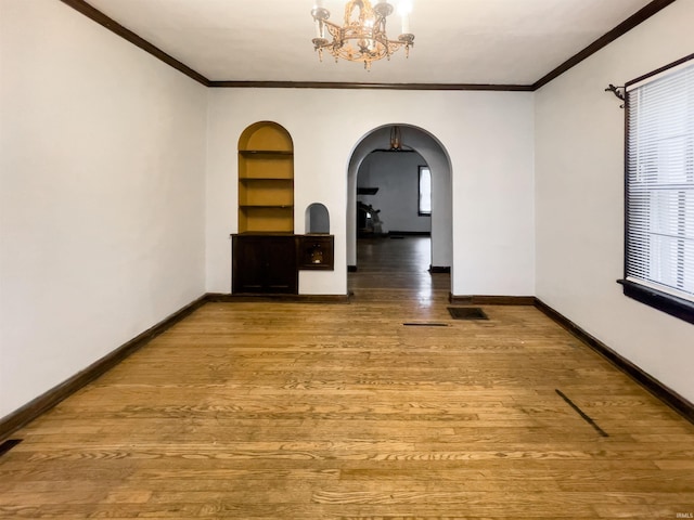 unfurnished room with built in shelves, wood-type flooring, crown molding, and an inviting chandelier