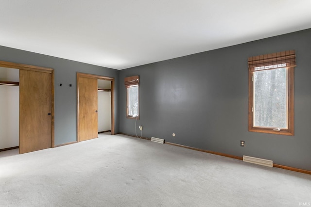 unfurnished bedroom featuring multiple closets and light colored carpet