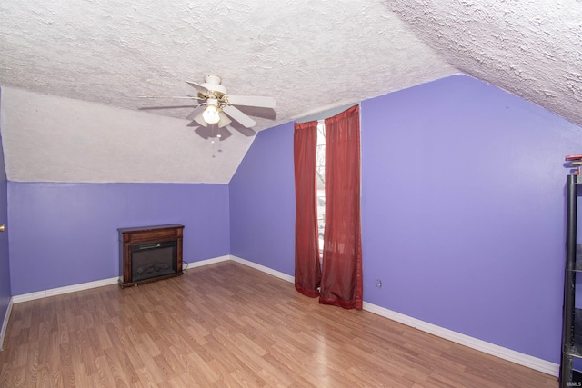 additional living space with vaulted ceiling, ceiling fan, a fireplace, a textured ceiling, and wood-type flooring