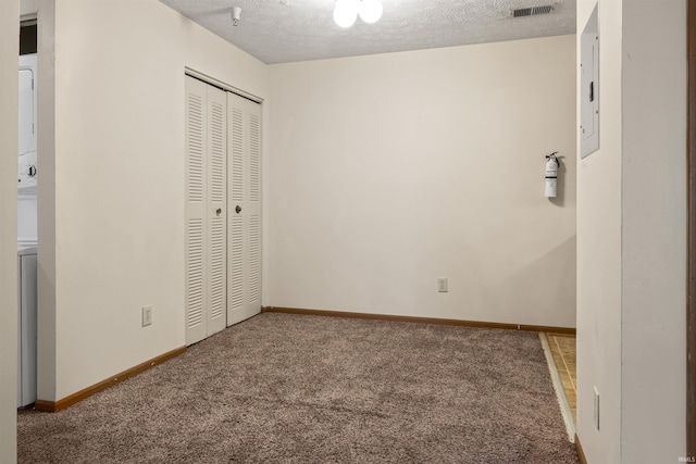 unfurnished bedroom featuring carpet flooring, a textured ceiling, electric panel, a closet, and stacked washer / drying machine