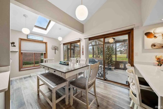 dining space with wood-type flooring, lofted ceiling with skylight, and ceiling fan