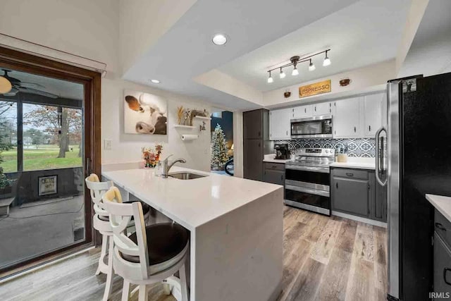 kitchen featuring appliances with stainless steel finishes, light wood-type flooring, a kitchen breakfast bar, gray cabinetry, and sink