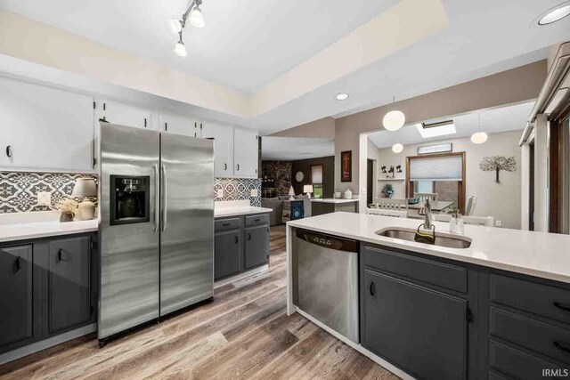 kitchen featuring sink, wood-type flooring, decorative backsplash, white cabinets, and appliances with stainless steel finishes