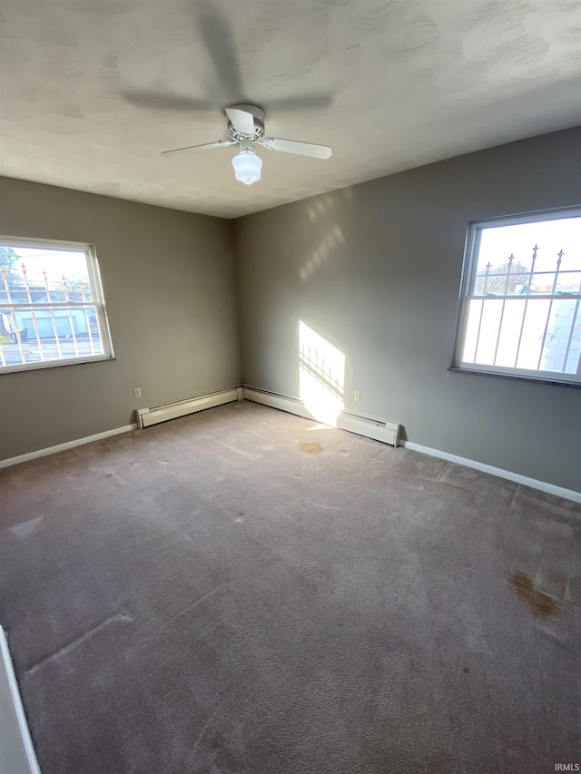 carpeted spare room with baseboard heating, a wealth of natural light, and ceiling fan