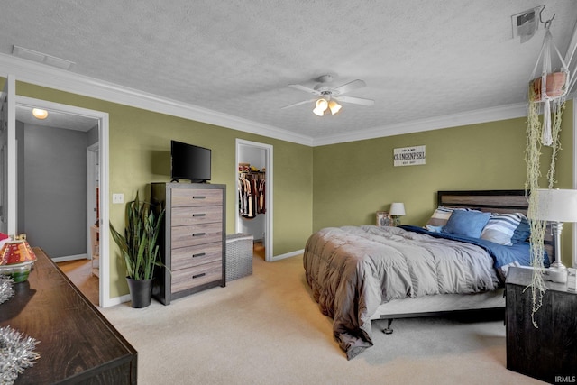 carpeted bedroom featuring a closet, a walk in closet, ceiling fan, and crown molding