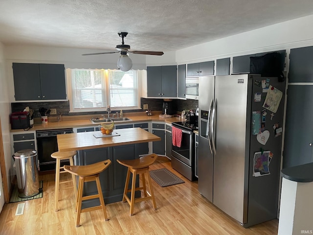 kitchen featuring ceiling fan, sink, stainless steel appliances, decorative backsplash, and a breakfast bar