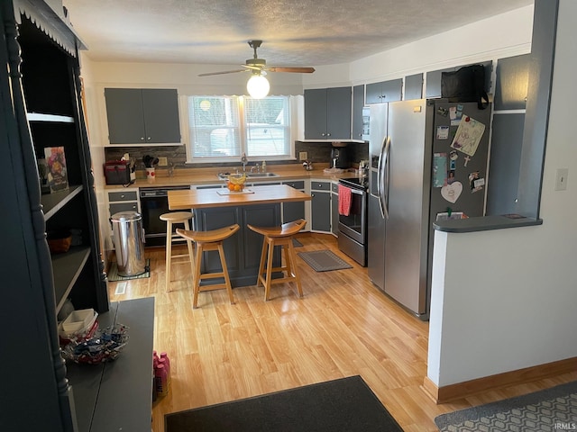 kitchen featuring a kitchen breakfast bar, stainless steel appliances, ceiling fan, sink, and light hardwood / wood-style floors