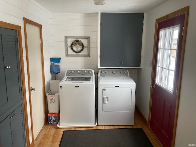 clothes washing area with light hardwood / wood-style floors, wood walls, cabinets, and separate washer and dryer