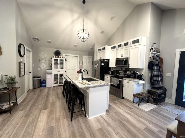 kitchen featuring light stone countertops, stainless steel appliances, sink, a center island with sink, and white cabinetry