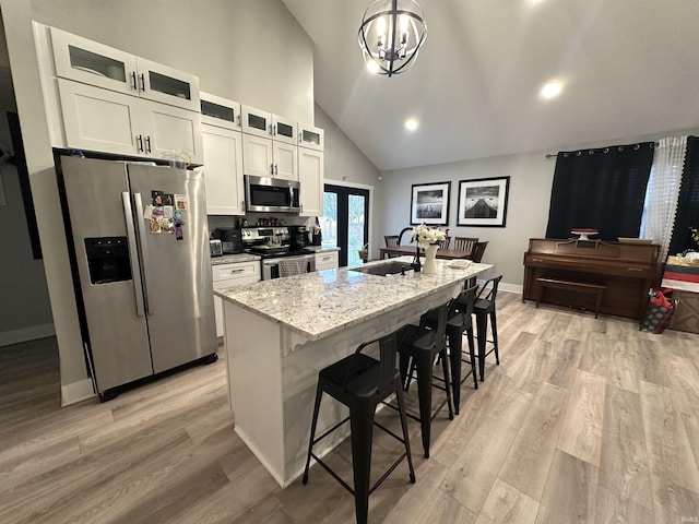 kitchen featuring light stone countertops, stainless steel appliances, a kitchen bar, a kitchen island with sink, and white cabinets