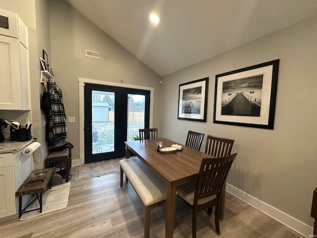 dining room with french doors, high vaulted ceiling, and light hardwood / wood-style floors