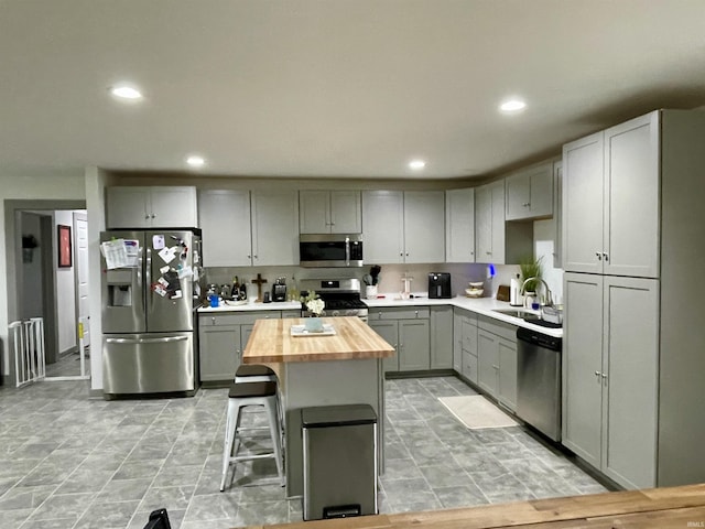 kitchen with a breakfast bar, sink, gray cabinets, appliances with stainless steel finishes, and butcher block countertops