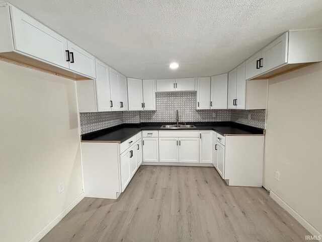 kitchen with backsplash, sink, light hardwood / wood-style flooring, a textured ceiling, and white cabinetry