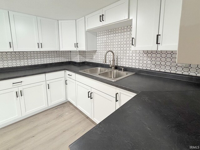 kitchen featuring white cabinets, backsplash, light wood-type flooring, and sink