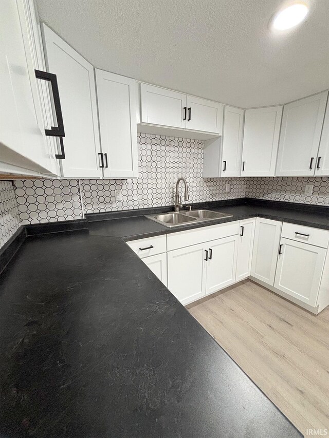 kitchen featuring white cabinets, a textured ceiling, sink, and light hardwood / wood-style flooring