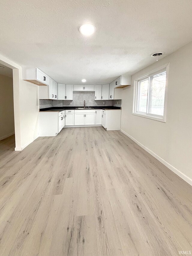 kitchen with sink, light wood-type flooring, a textured ceiling, tasteful backsplash, and white cabinetry