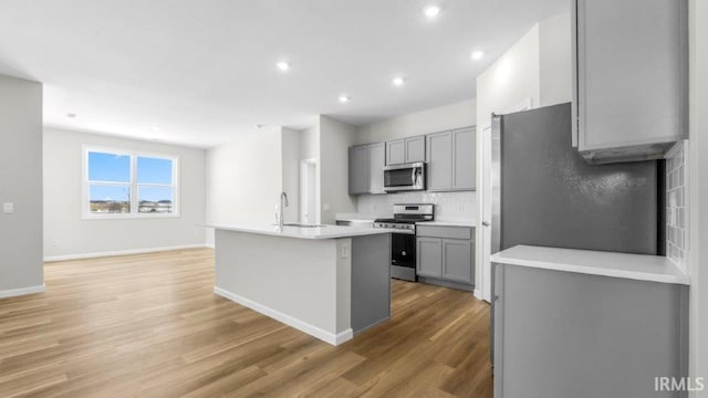 kitchen featuring stainless steel appliances, a kitchen island with sink, gray cabinets, and light countertops