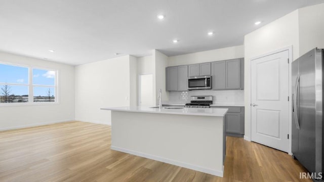 kitchen with a center island with sink, gray cabinets, light countertops, appliances with stainless steel finishes, and a sink