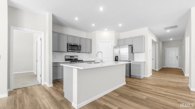 kitchen featuring light countertops, visible vents, gray cabinetry, appliances with stainless steel finishes, and a kitchen island with sink