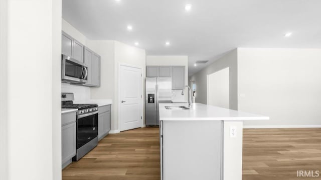 kitchen featuring an island with sink, gray cabinets, stainless steel appliances, light countertops, and a sink