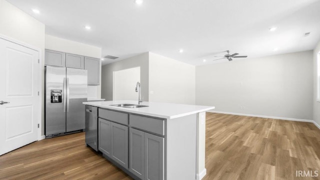 kitchen with a center island with sink, gray cabinets, stainless steel appliances, light countertops, and a sink