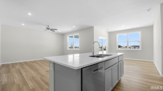 kitchen featuring dishwasher, a kitchen island with sink, light countertops, gray cabinetry, and a sink