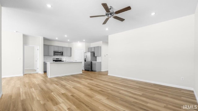 kitchen with open floor plan, a kitchen island with sink, stainless steel appliances, light countertops, and gray cabinetry