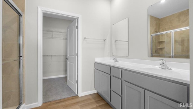 bathroom featuring double vanity, a stall shower, wood finished floors, a spacious closet, and a sink