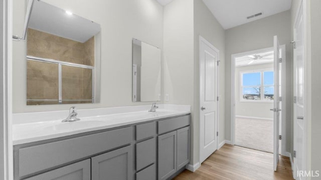 full bathroom featuring wood finished floors, a sink, visible vents, a tile shower, and double vanity
