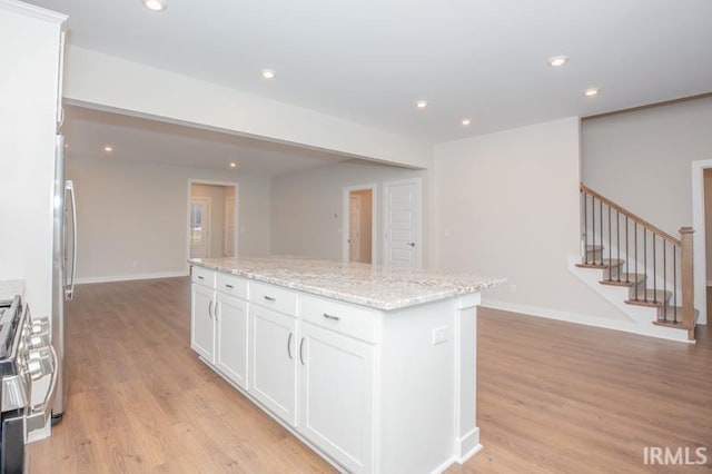 kitchen with light stone countertops, appliances with stainless steel finishes, light wood-type flooring, a kitchen island, and white cabinetry