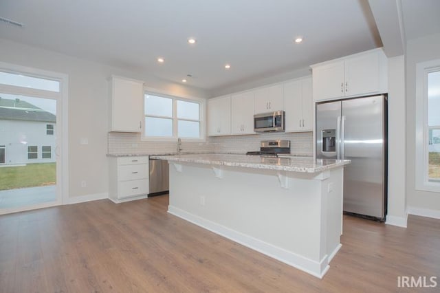 kitchen with a kitchen island, light stone counters, white cabinetry, and appliances with stainless steel finishes