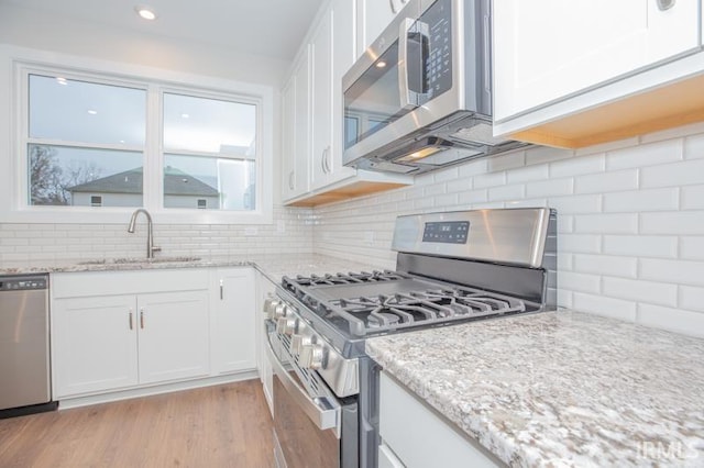 kitchen with appliances with stainless steel finishes, backsplash, sink, light hardwood / wood-style floors, and white cabinetry