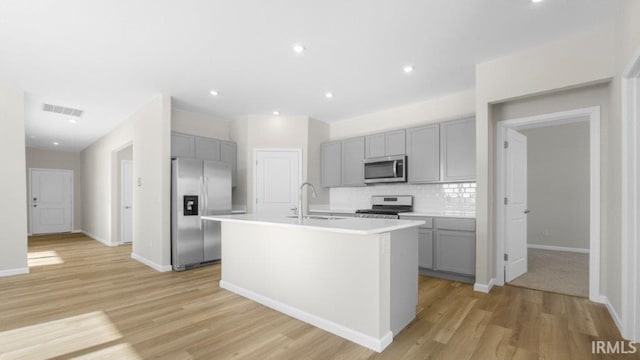 kitchen with stainless steel appliances, a sink, visible vents, light countertops, and an island with sink