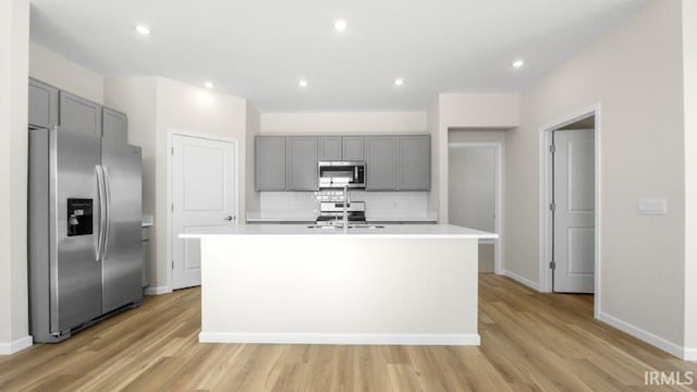 kitchen with light countertops, appliances with stainless steel finishes, an island with sink, and gray cabinetry