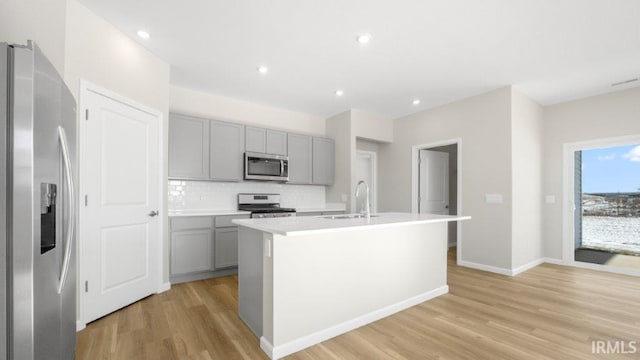 kitchen featuring a kitchen island with sink, stainless steel appliances, a sink, light countertops, and tasteful backsplash