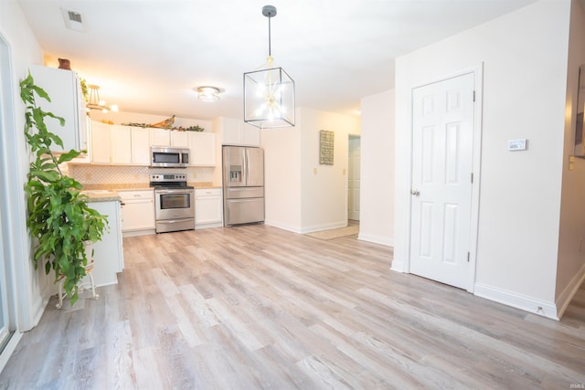 kitchen with light wood-type flooring, tasteful backsplash, stainless steel appliances, pendant lighting, and white cabinets